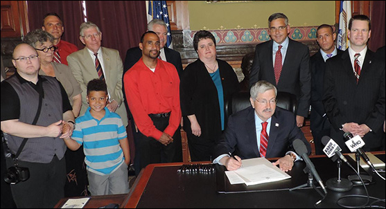 Photograph (above): Iowa Gov. Terry Branstad signs a bill May 30, 2014, reforming the state’s laws HIV transmission laws (courtesy Community HIV and Hepatitis Advocates of Iowa Network). See sidebar for links to related resources.